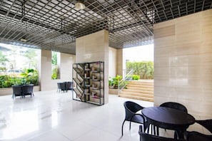 A modern indoor area with a geometric bookshelf, black chairs, and a tiled floor.