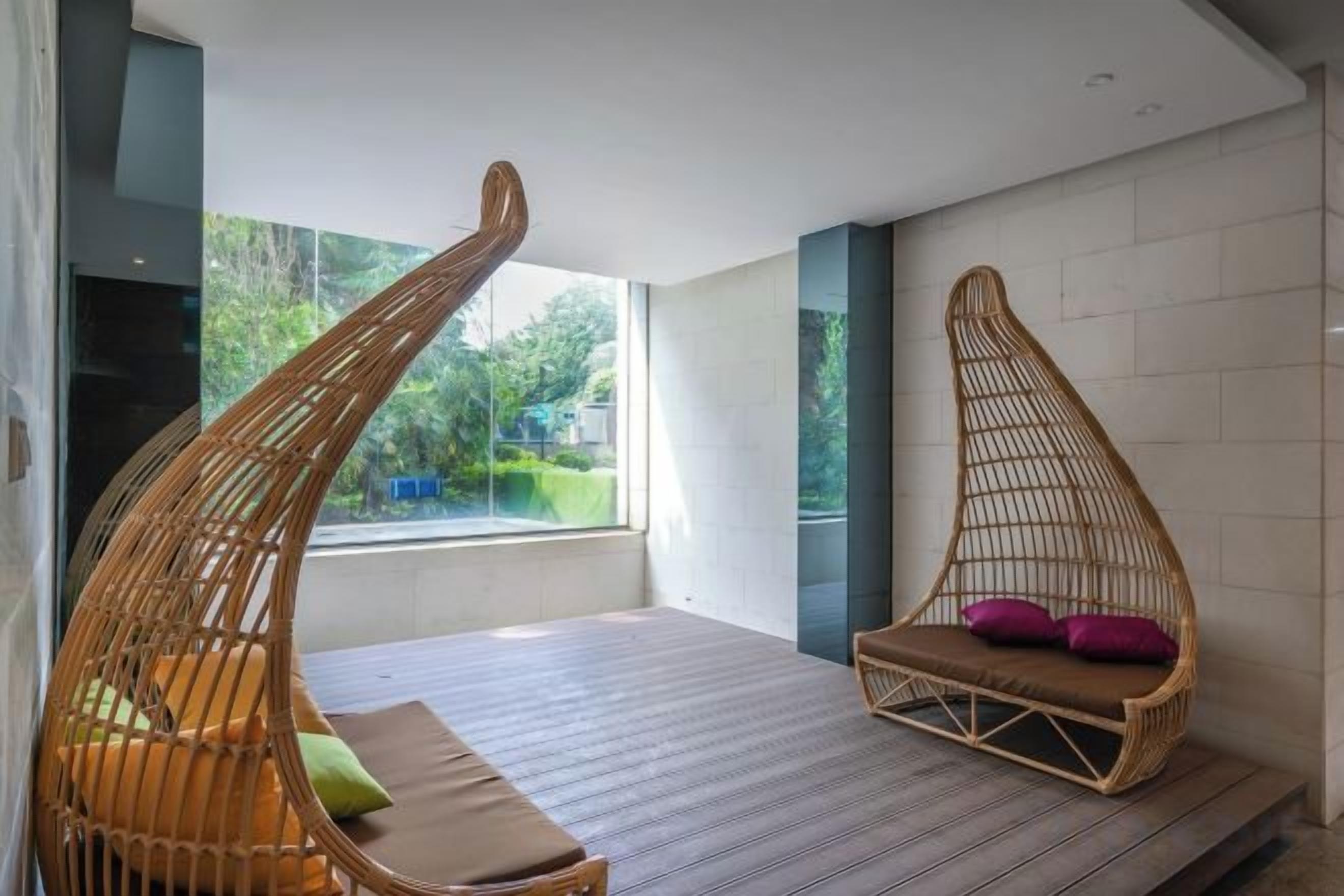 A modern room with a large window, a bed with a striped mattress, and two wicker chairs with cushions.