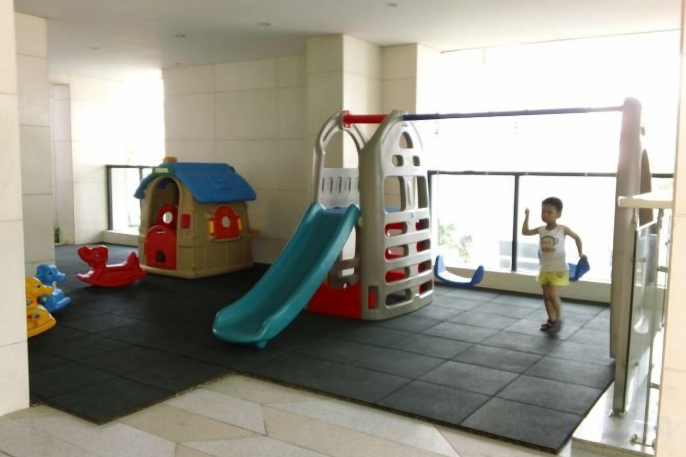 A children's play area with a slide and climbing structure, a small house, and a child playing.