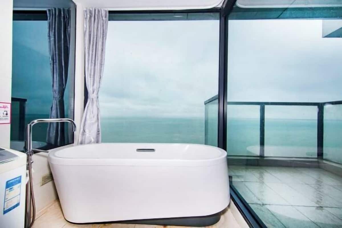 A modern bathroom with a large bathtub, a glass shower enclosure, and a view of the sea.