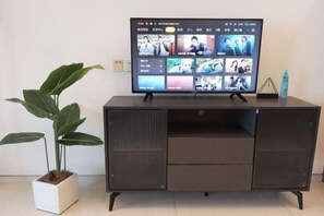 Un téléviseur à écran plat posé sur un meuble de couleur sombre, avec une plante à côté.
