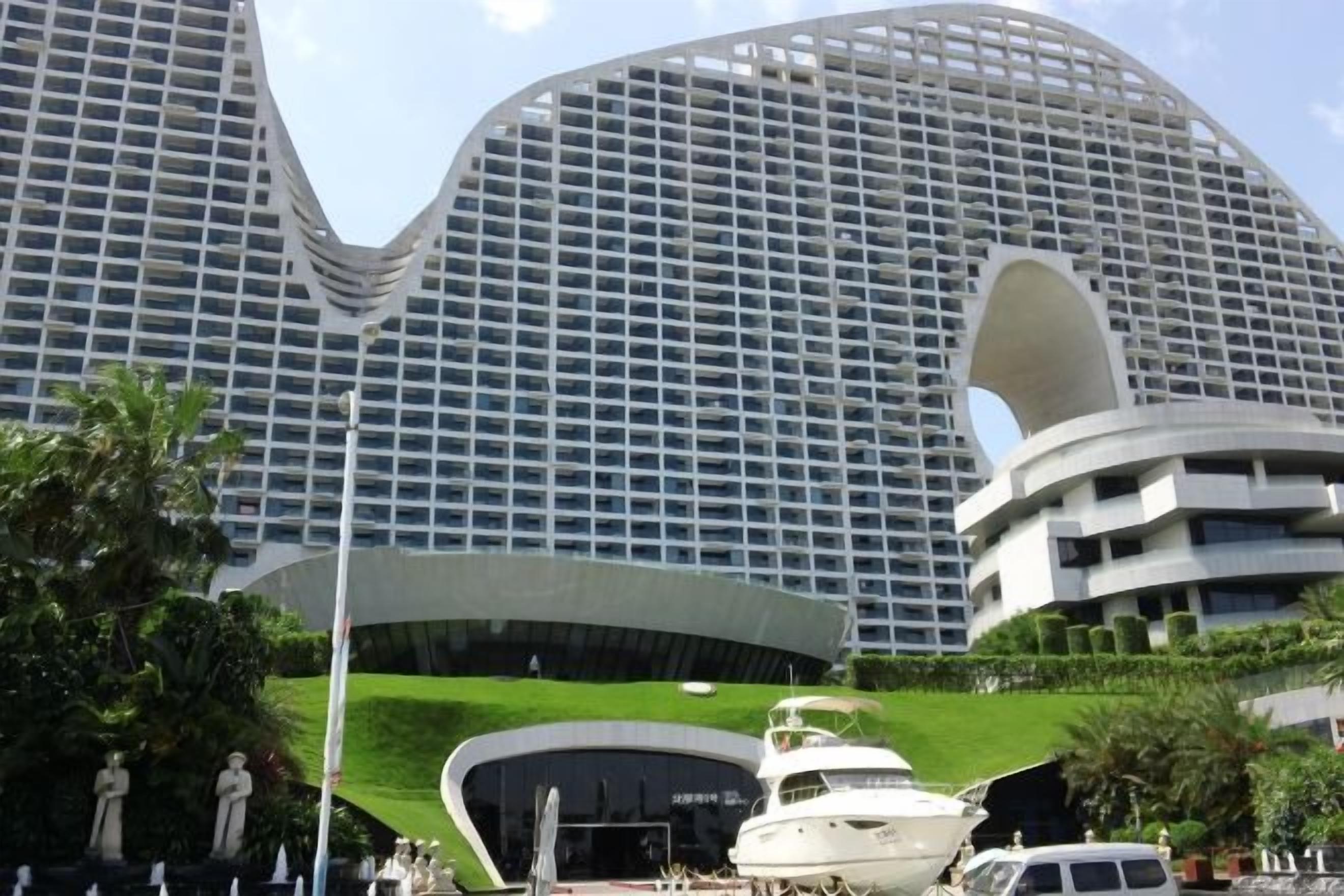 A modern building with a unique curved facade, a large entrance, and a yacht docked nearby.