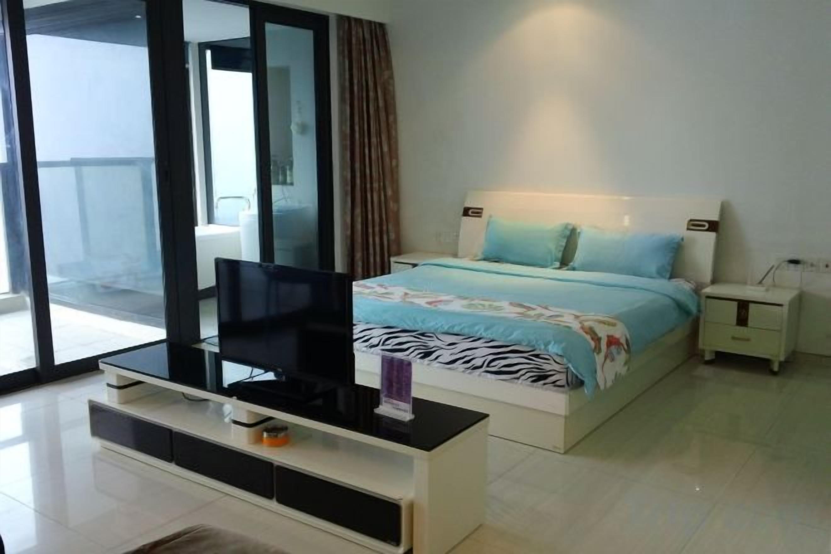 Un dormitorio con una cama, un televisor sobre un mueble bajo, una mesita de noche y un ventanal corredero al exterior.