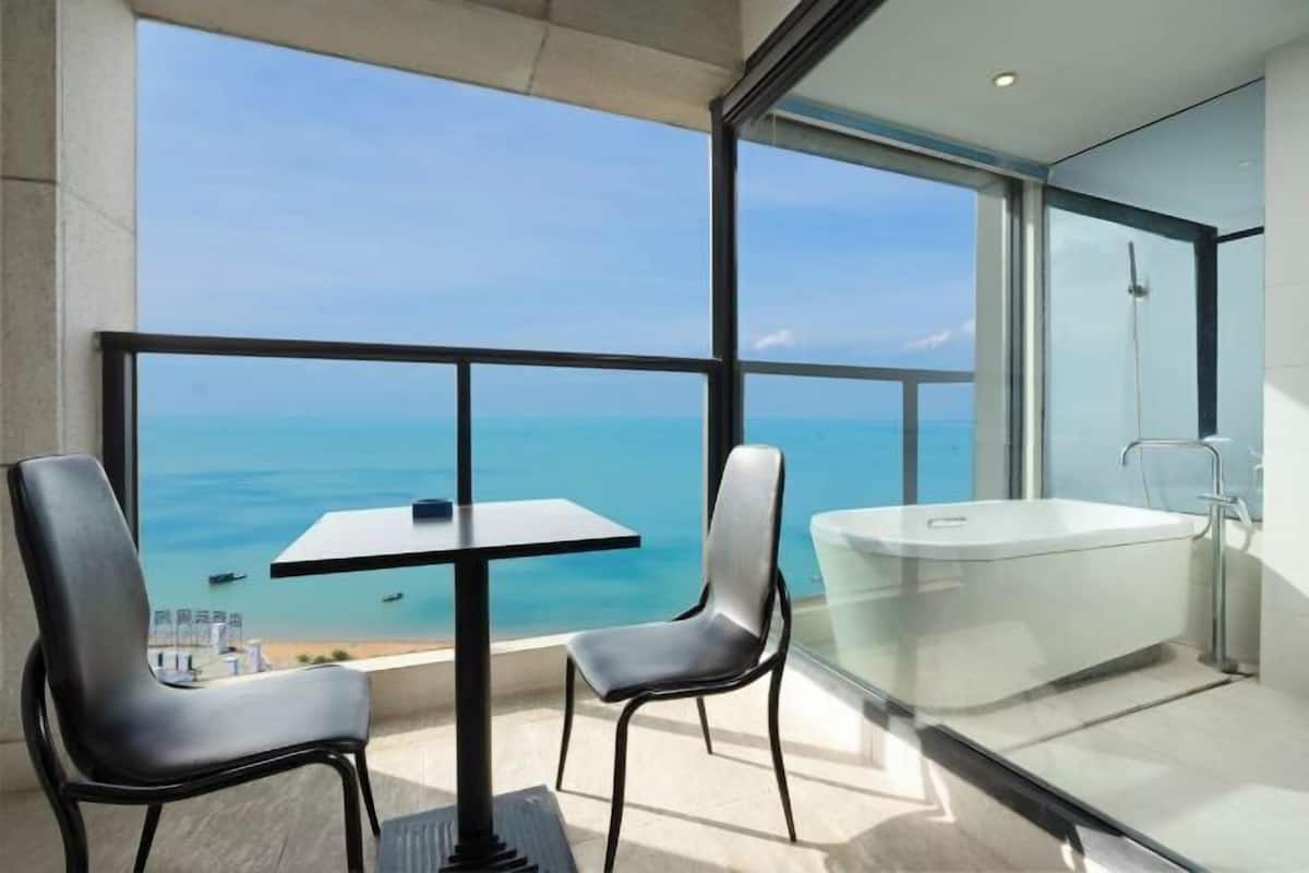 A modern bathroom with a glass-enclosed shower, a bathtub, and a view of the ocean.