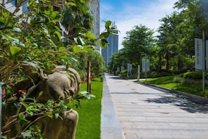 A pathway lined with greenery and a stone sculpture, leading towards a modern building.