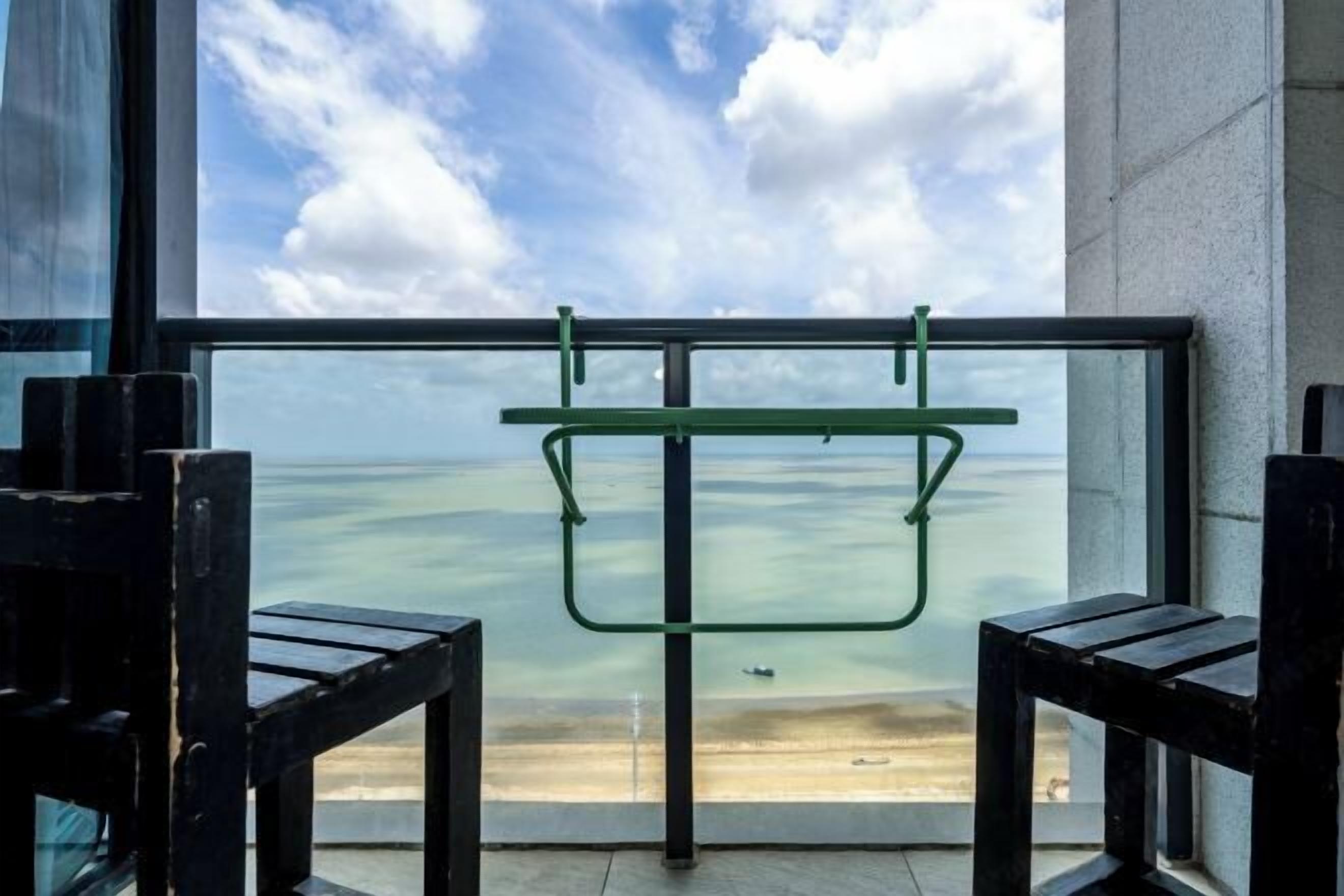 A balcony with a view of the sea, a metal rack, and two wooden chairs.