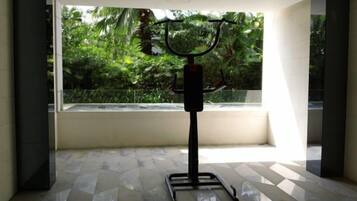 A gym area with a stationary bike and a weight bench, large windows with a view of greenery outside.