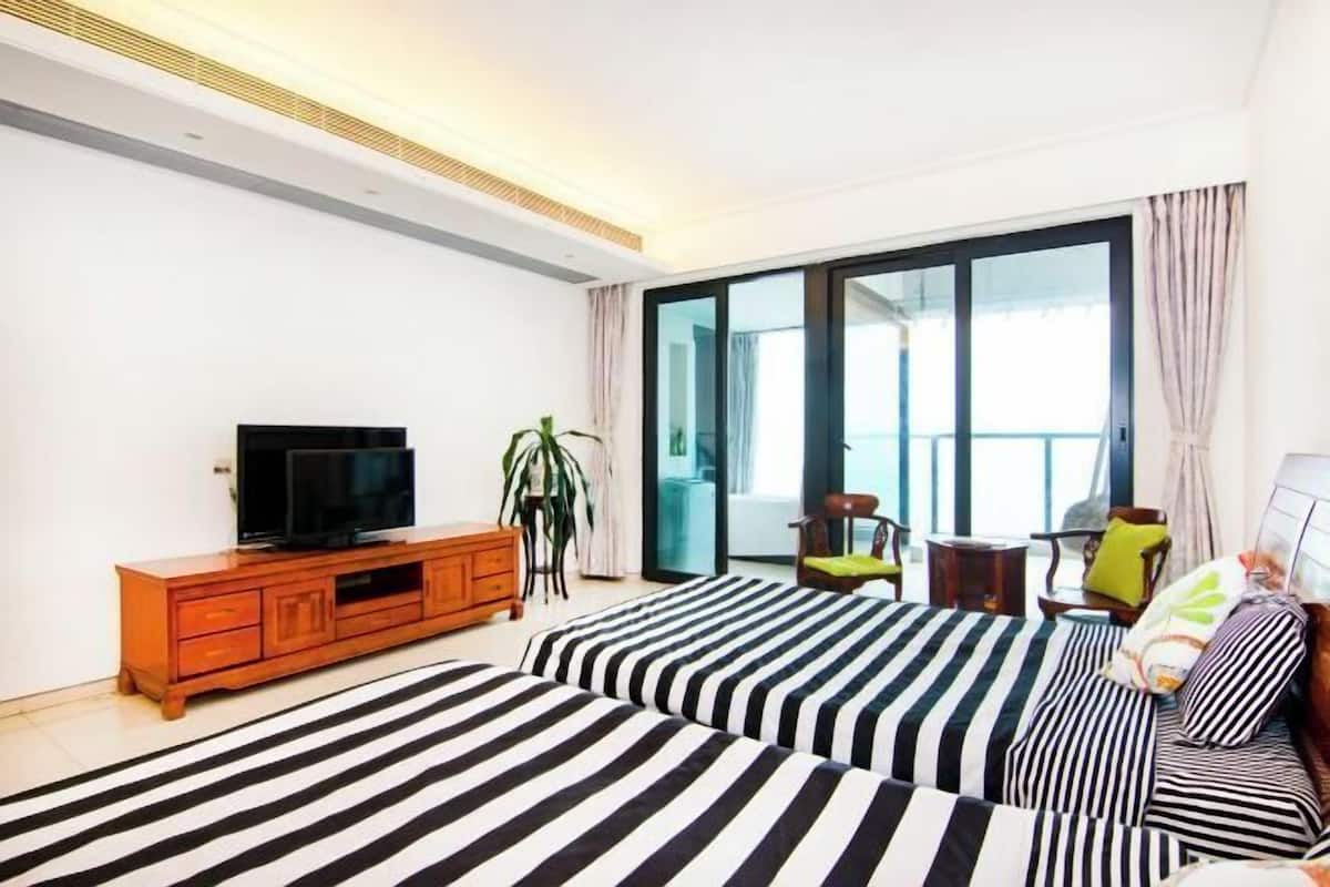 A hotel room with two beds, a TV, a plant, and a balcony with a view.