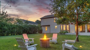 A backyard with a fire pit surrounded by Adirondack chairs, a house in the background, and a tree. - Modern Home: Hot-Tub, Fire-Pit, Sleeps12, Pets ok (Indianapolis)