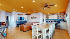A spacious living area with a wooden ceiling, a dining table with chairs, a sofa, and a television mounted on the wall. - OV10 Golf Cart Included, Shared Pool, Pet Friendly, Parking for 3 (Port Aransas)