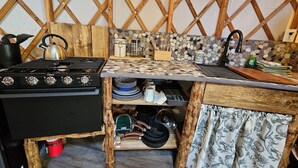 A rustic kitchen with a wooden stove, a tiled backsplash, and a wooden table. - Premium Comfort in the Wilderness (Nabesna)
