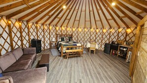 A cozy yurt interior with a central bed, wooden furniture, and a dining area. - Premium Comfort in the Wilderness (Nabesna)