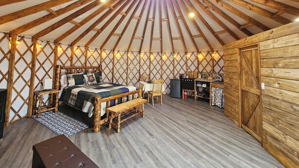 A cozy yurt interior with a central bed, a small table, and a bench. - Premium Comfort in the Wilderness (Nabesna)