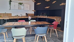 A modern kitchen with a built-in stove, a dining area with wooden tables and chairs, and a black wall with wooden shelves. - Figueira's House by the Atlantic (Ponta do Sol)