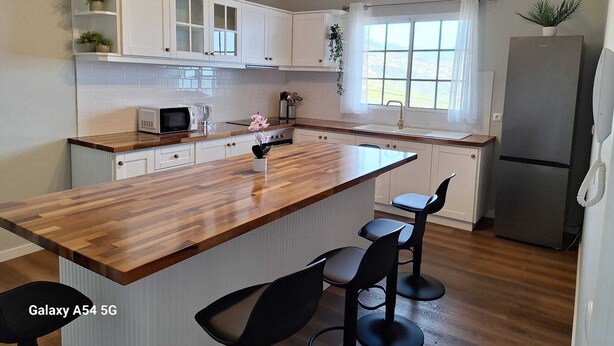 A modern kitchen with white cabinets, a wooden island, and a stainless steel refrigerator. - Figueira's House by the Atlantic (Ponta do Sol)