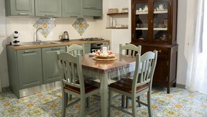 Une cuisine avec des meubles de rangement verts, une table à manger en bois avec des chaises, un meuble avec des portes en verre et un sol à motifs.