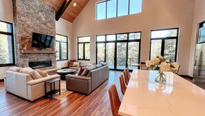 A spacious living room with a stone fireplace, large windows, and a dining area.