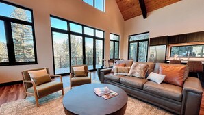 A spacious living room with large windows, a leather sofa, two armchairs, and a round coffee table.