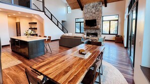 A spacious living area with a large wooden dining table, a stone fireplace, and a modern kitchen with a built-in island.