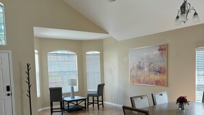 Un vaste espace dédié à la salle à manger, avec un plafond haut, de grandes fenêtres et un tableau accroché au mur.