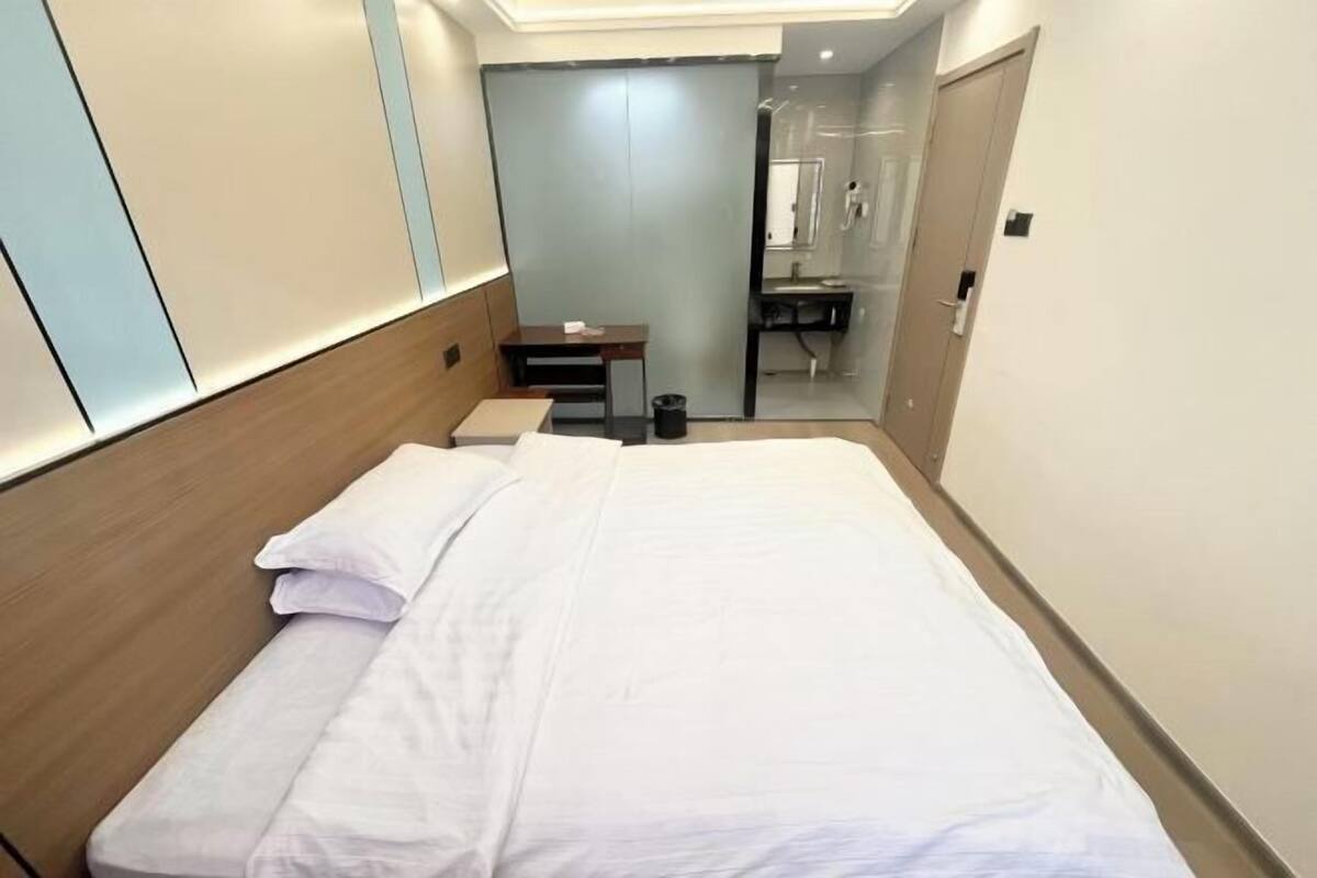 Een hotelkamer met een bed, een bureau, een prullenbak en een badkamer, zichtbaar door een glazen deur.