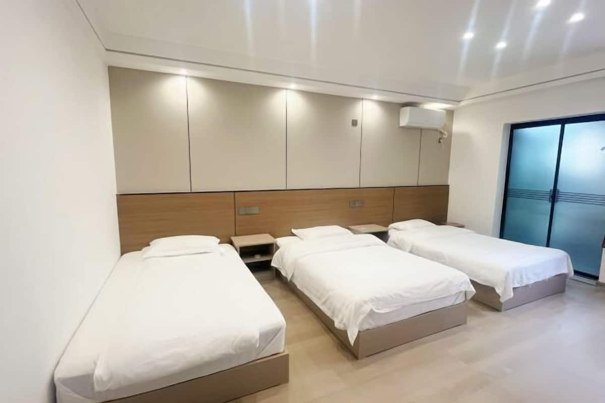 Een hotelkamer met drie eenpersoonsbedden, een houten hoofdbord, een groot raam en een schuifpui.