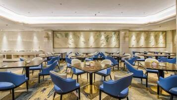 A hotel dining area with round tables and blue chairs, a marble floor, and a large wall with decorative panels.