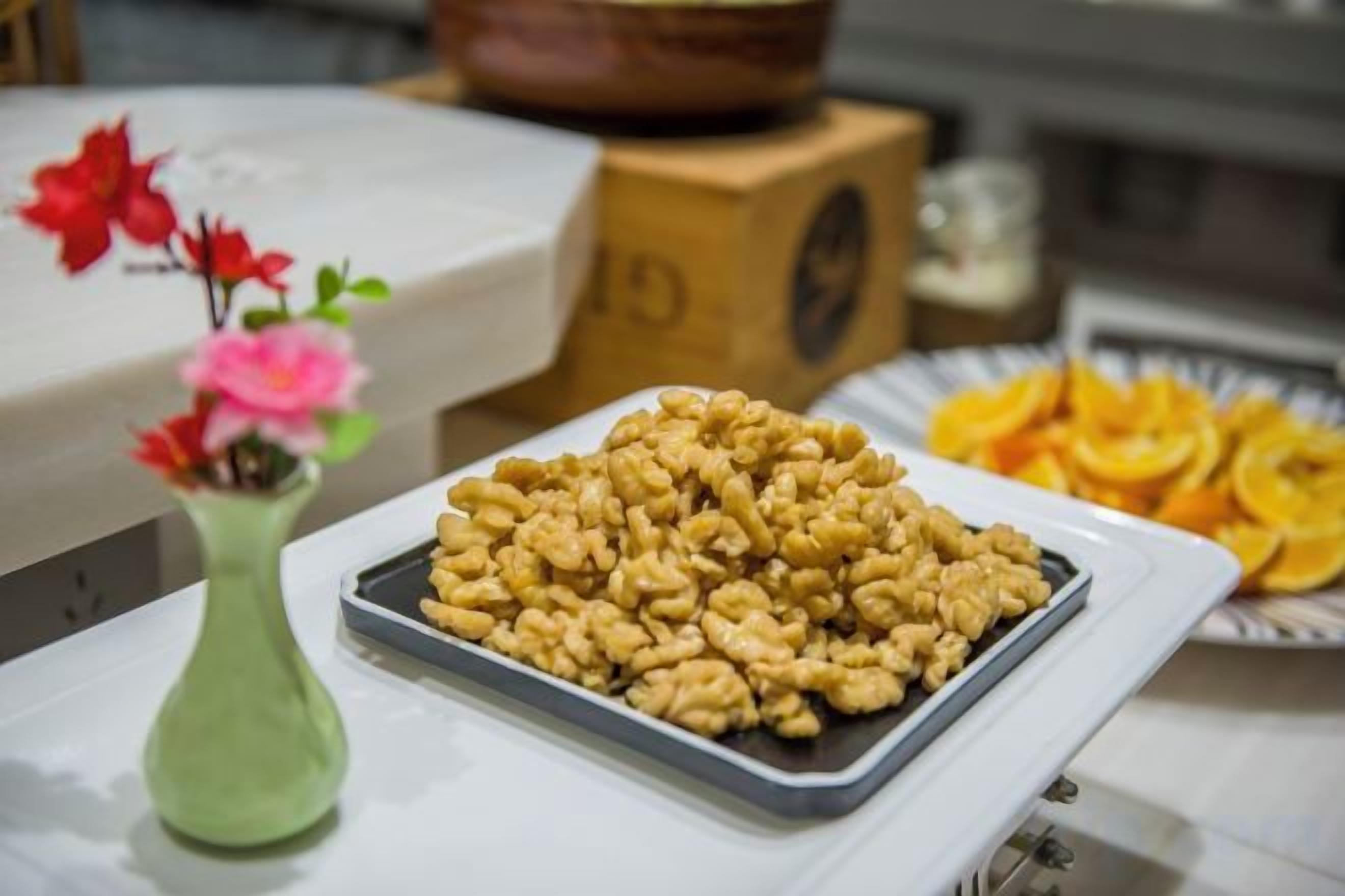 Een schaal met walnoten op een tafel, met een bloevas en een bord gedroogde sinaasappelpartjes.