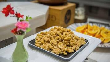 Een schaal met walnoten op een tafel, met een bloevas en een bord gedroogde sinaasappelpartjes.