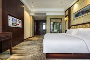 Habitación de hotel con una cama grande, un escritorio, un televisor montado en la pared y un cuadro enmarcado.