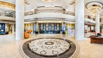 A spacious lobby with a central circular floor design, multiple reception desks, and a high ceiling with chandeliers.
