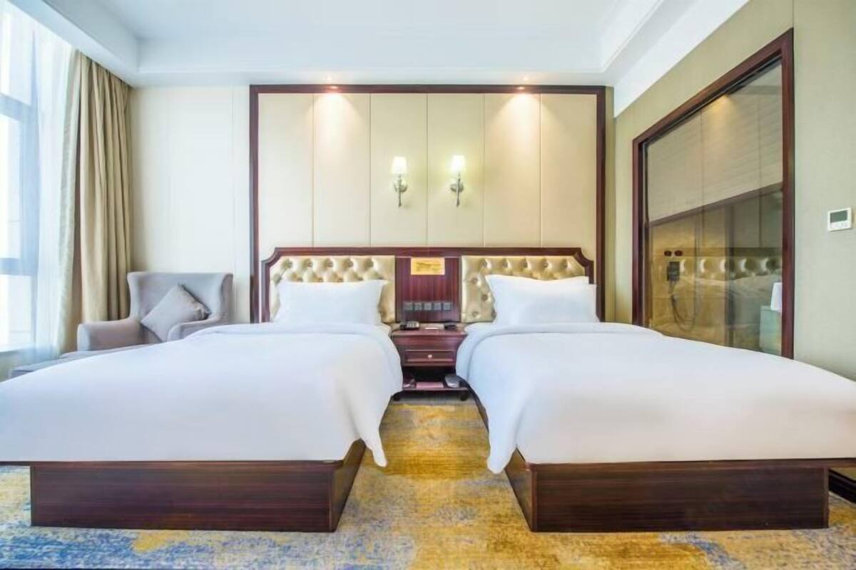 A hotel room with two beds, a large mirror, and a view of the city.