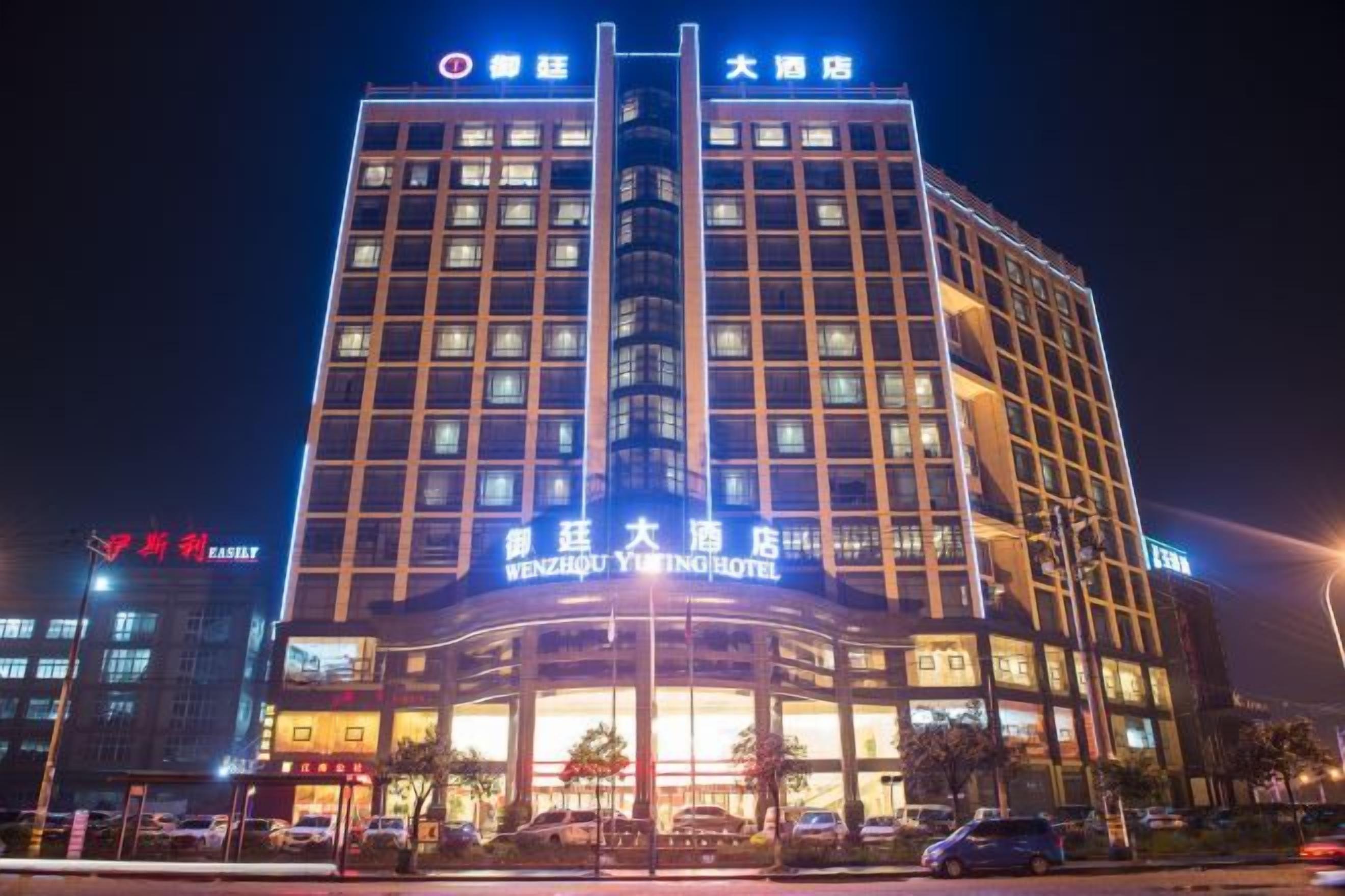 Un hotel de varios pisos con señalización iluminada, una entrada destacada y un área de estacionamiento al frente.