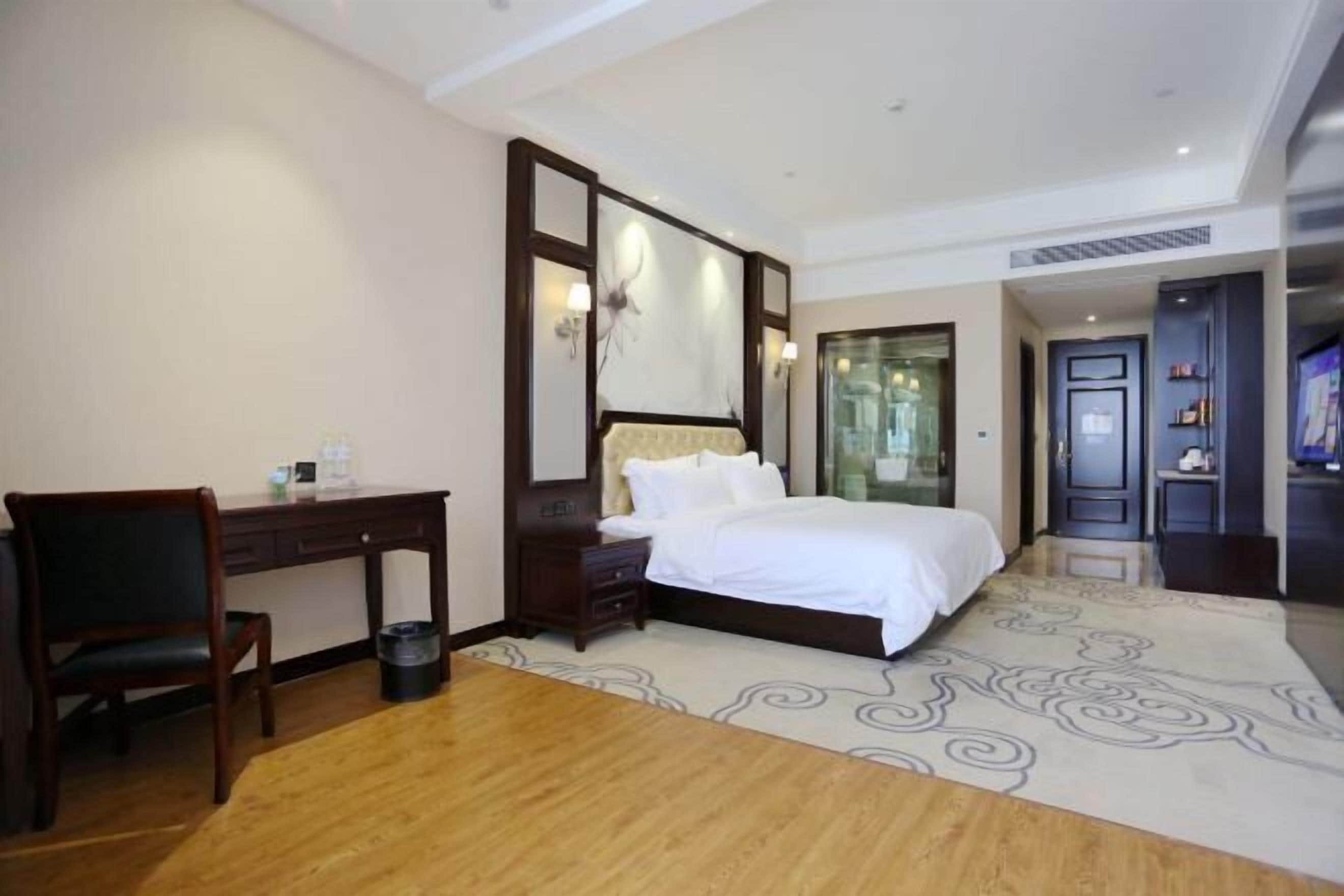 A hotel room with a bed, a desk, a chair, and a large mirror.