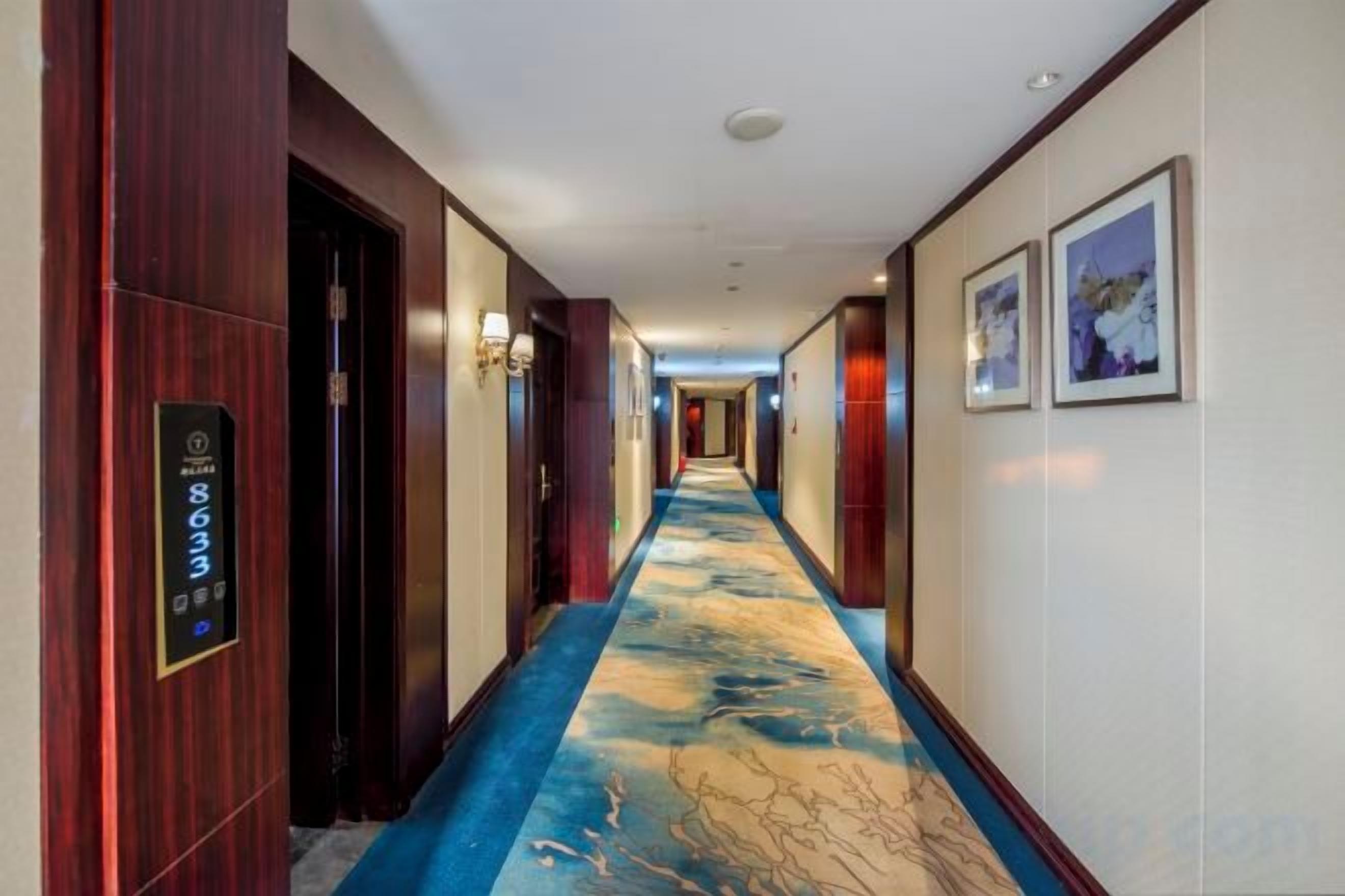 A hotel corridor with a blue carpet, wooden doors, and wall-mounted light fixtures.