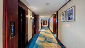 A hotel corridor with a blue carpet, wooden doors, and wall-mounted light fixtures.