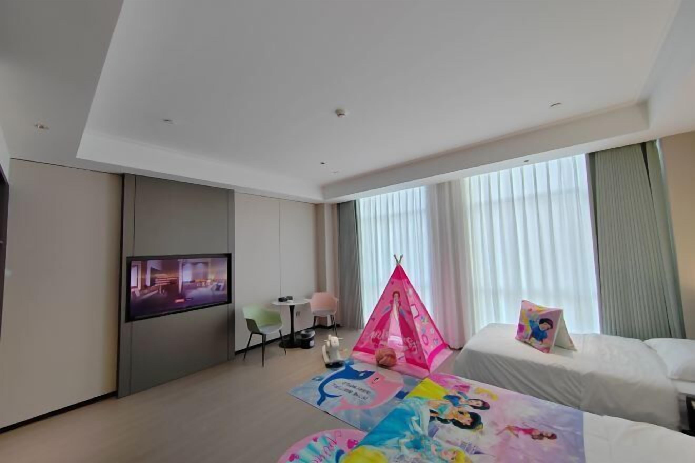 A hotel room with a flat-screen TV, a tent, and a bed with a colorful blanket.