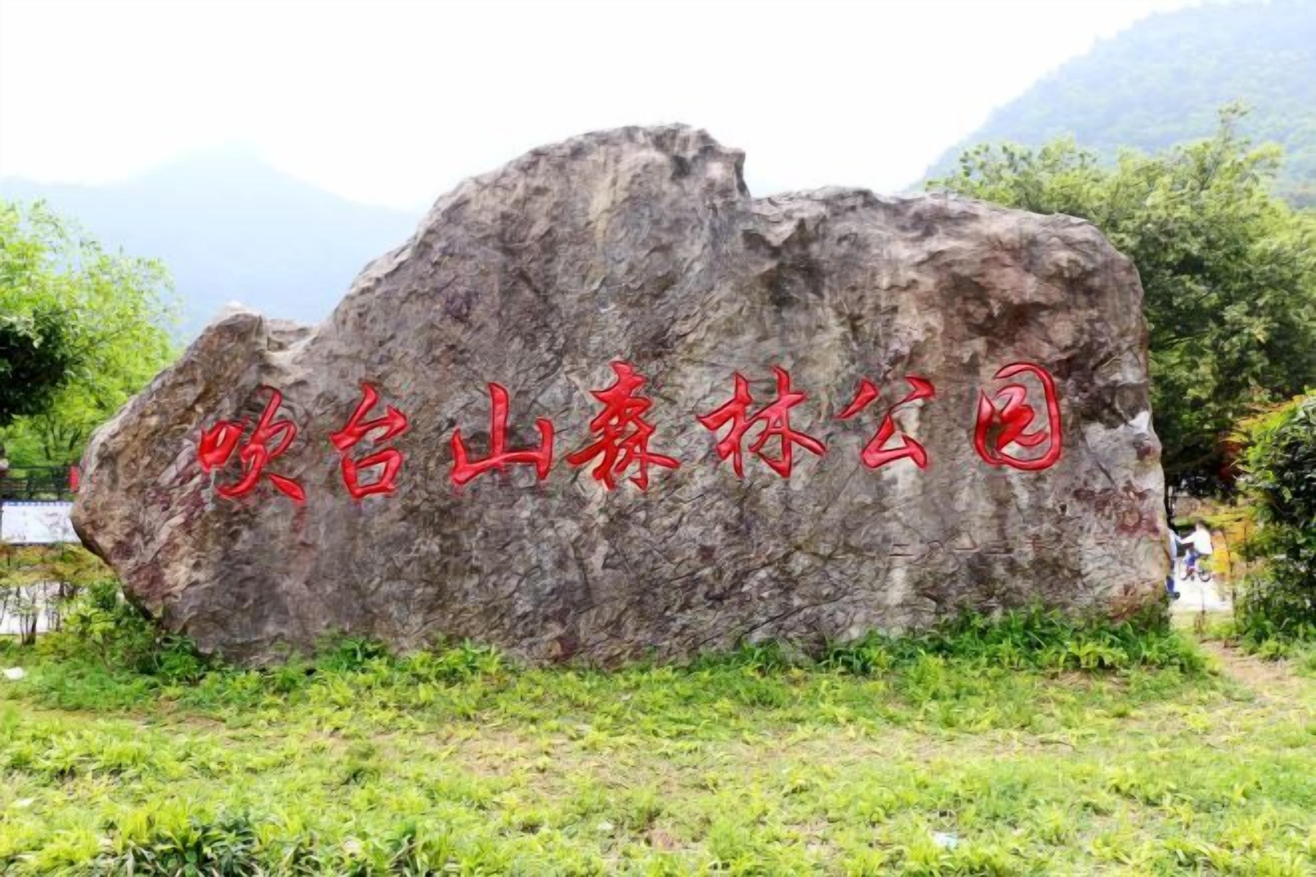A large rock with red text, surrounded by greenery and a mountain in the background.