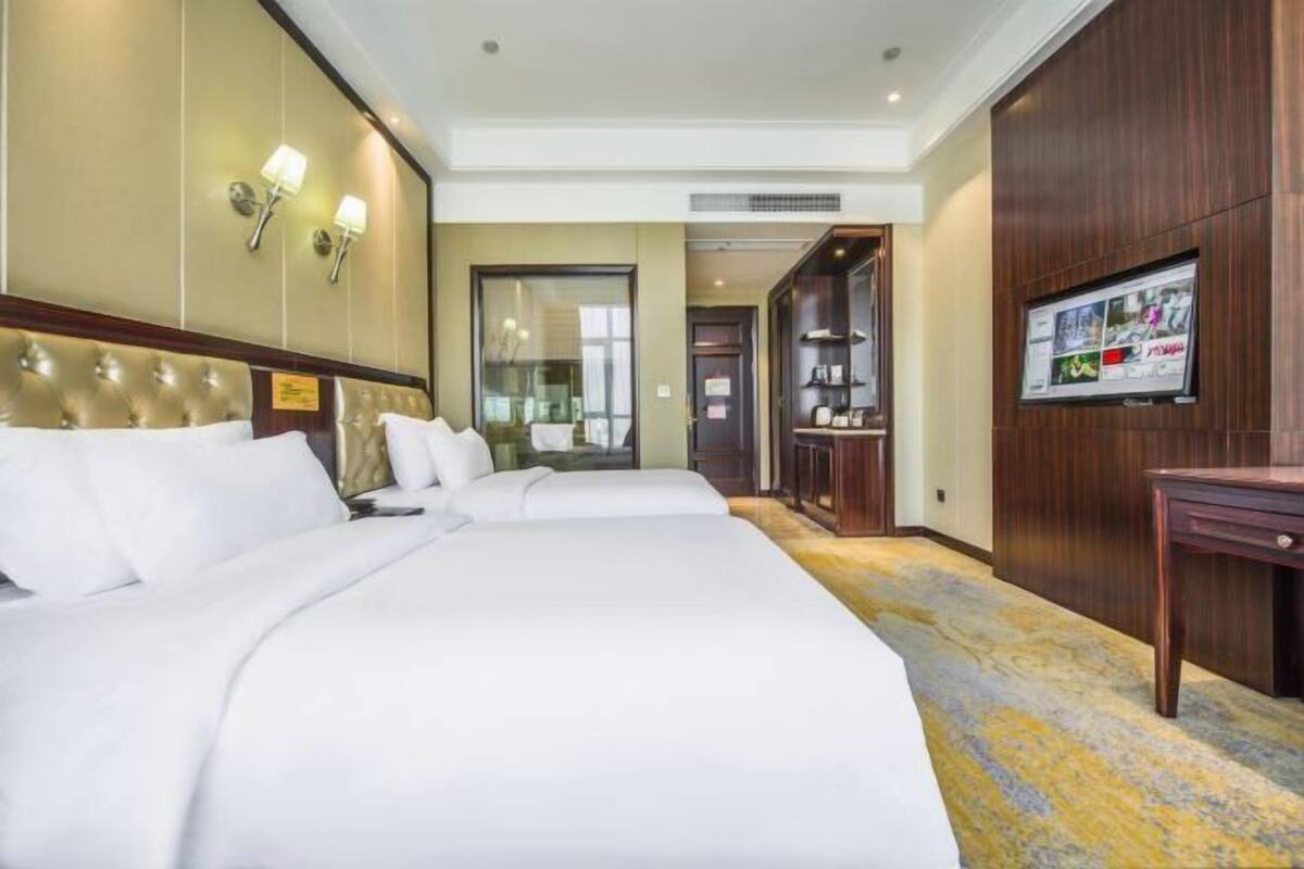 A hotel room with a large bed, a television, and a wooden cabinet.