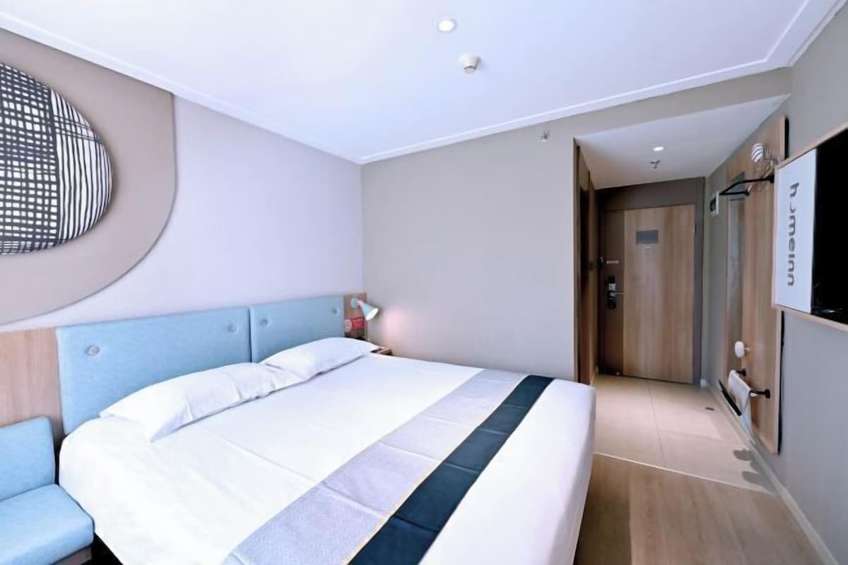 A modern hotel room with a large bed, a seating area, a TV, and a door leading to a bathroom.
