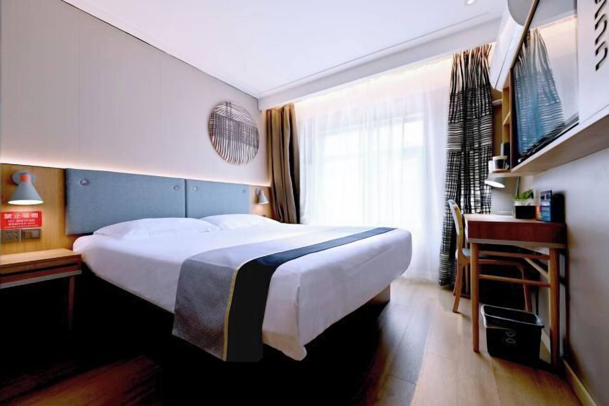 A hotel room with a bed, bedside table, lamp, and a desk with a chair.