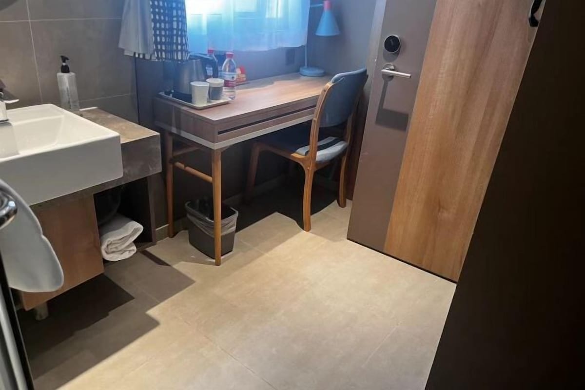 A compact bathroom with a sink, toilet, and a small desk with a chair.