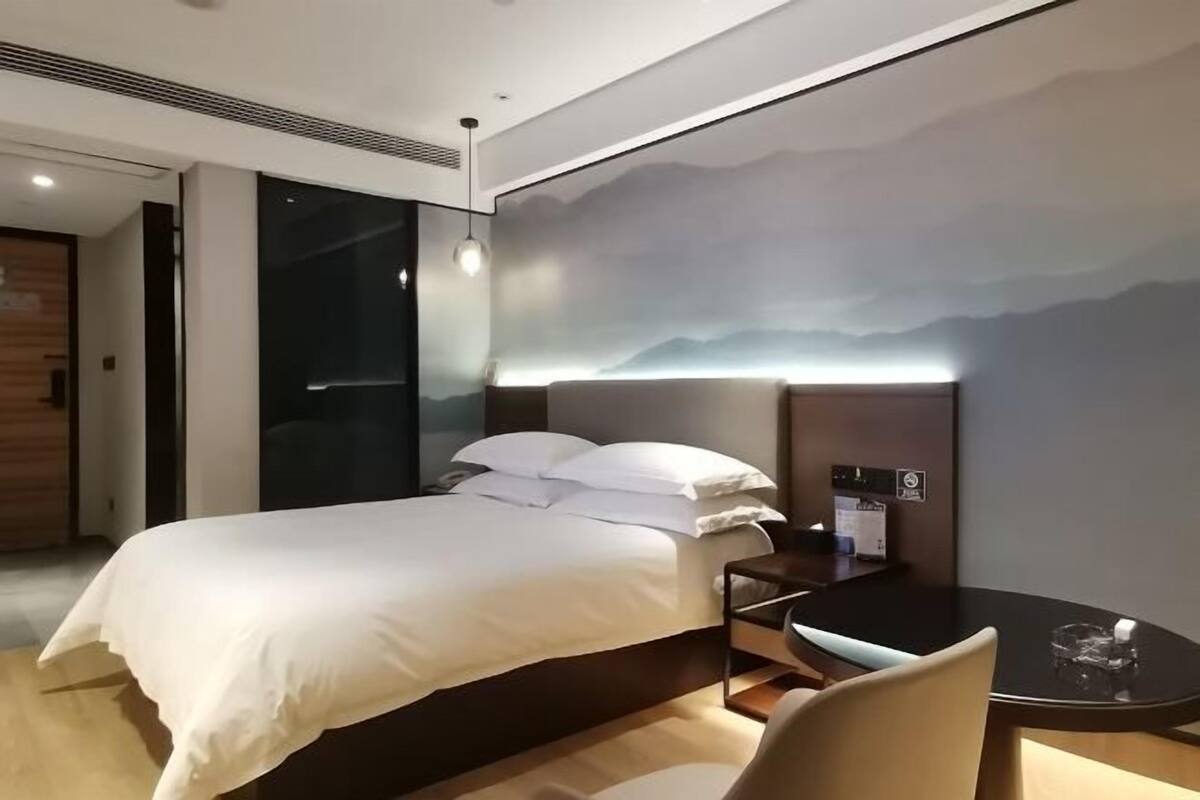 A modern hotel room with a bed, bedside table, chair, and a wall-mounted TV.