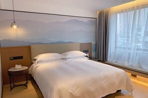 Hotelkamer met een bed, nachtkastje met lamp, raam met gordijnen, en een muur met een berglandschap.