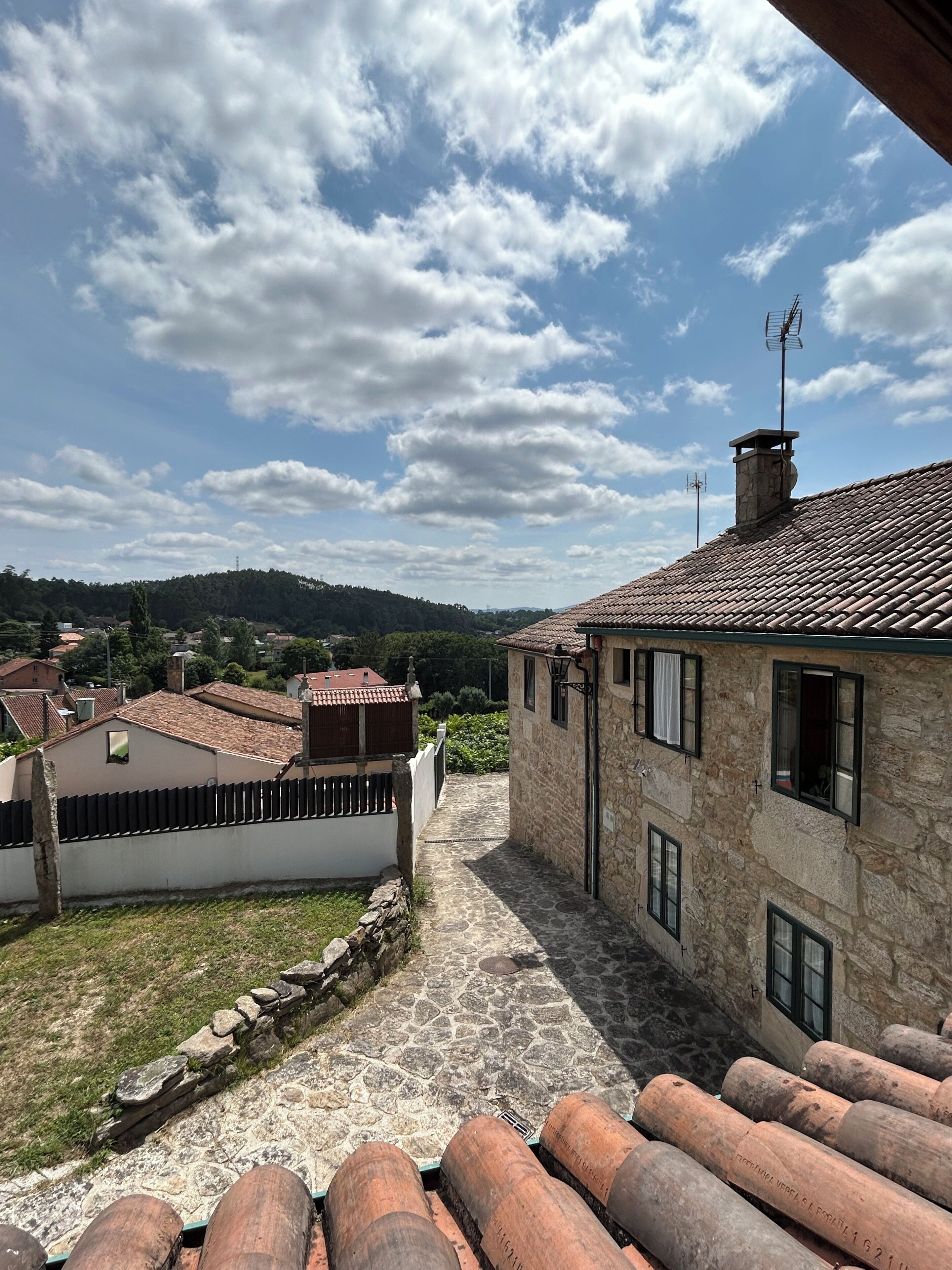 Un edificio de piedra con techo de tejas, un camino de piedra y vistas del paisaje circundante.