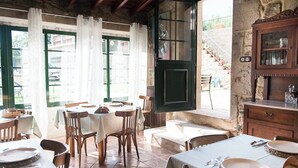 A dining area with tables set for meals, a stone wall, and a view of the outside. - CASA DE COSTOIA (Ames)