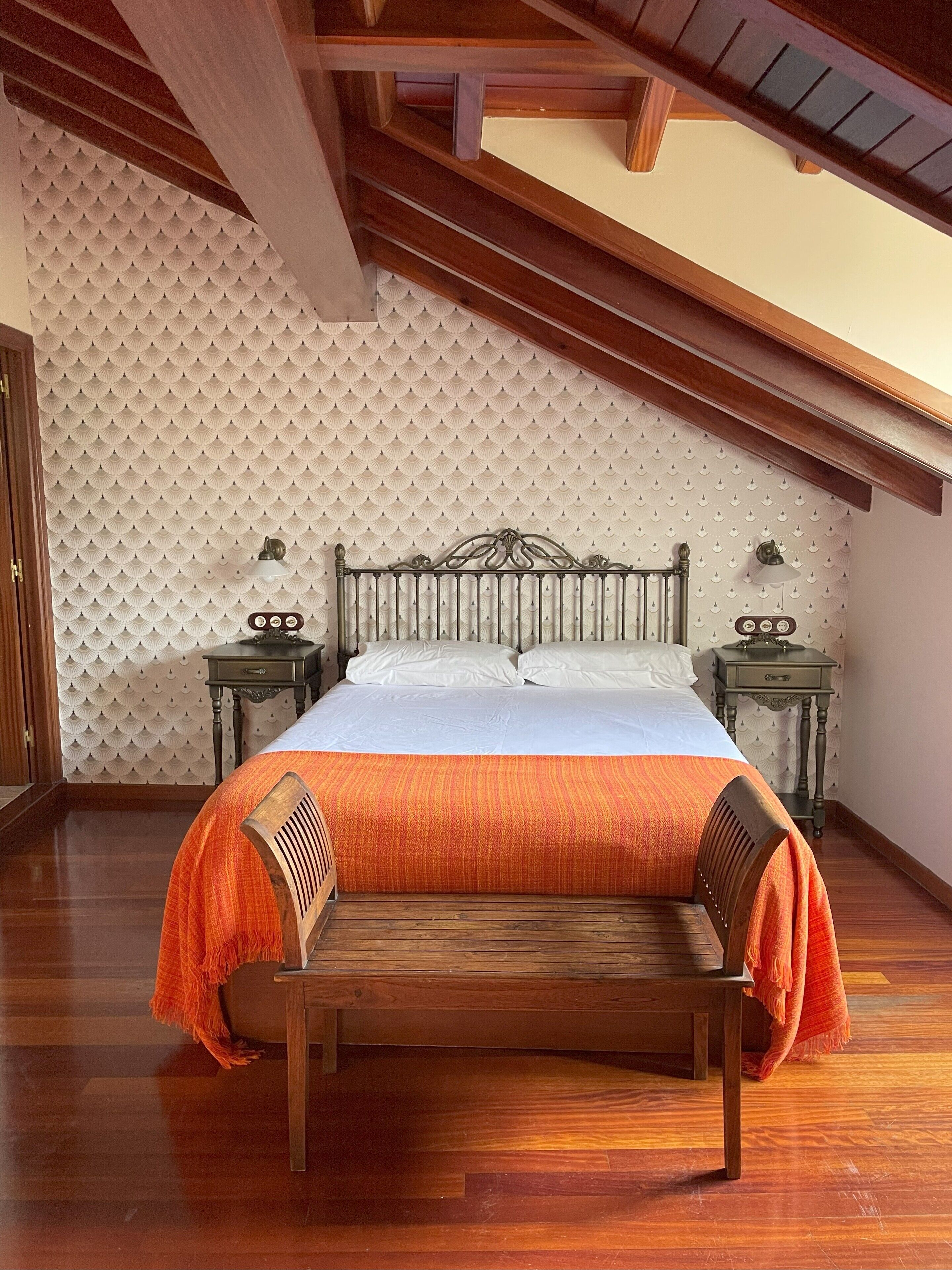 A bedroom with a wooden bed, two bedside tables, a bench, and a patterned wall.