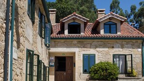 A stone building with a tiled roof, a wooden door, and green shutters. - CASA DE COSTOIA (Ames)