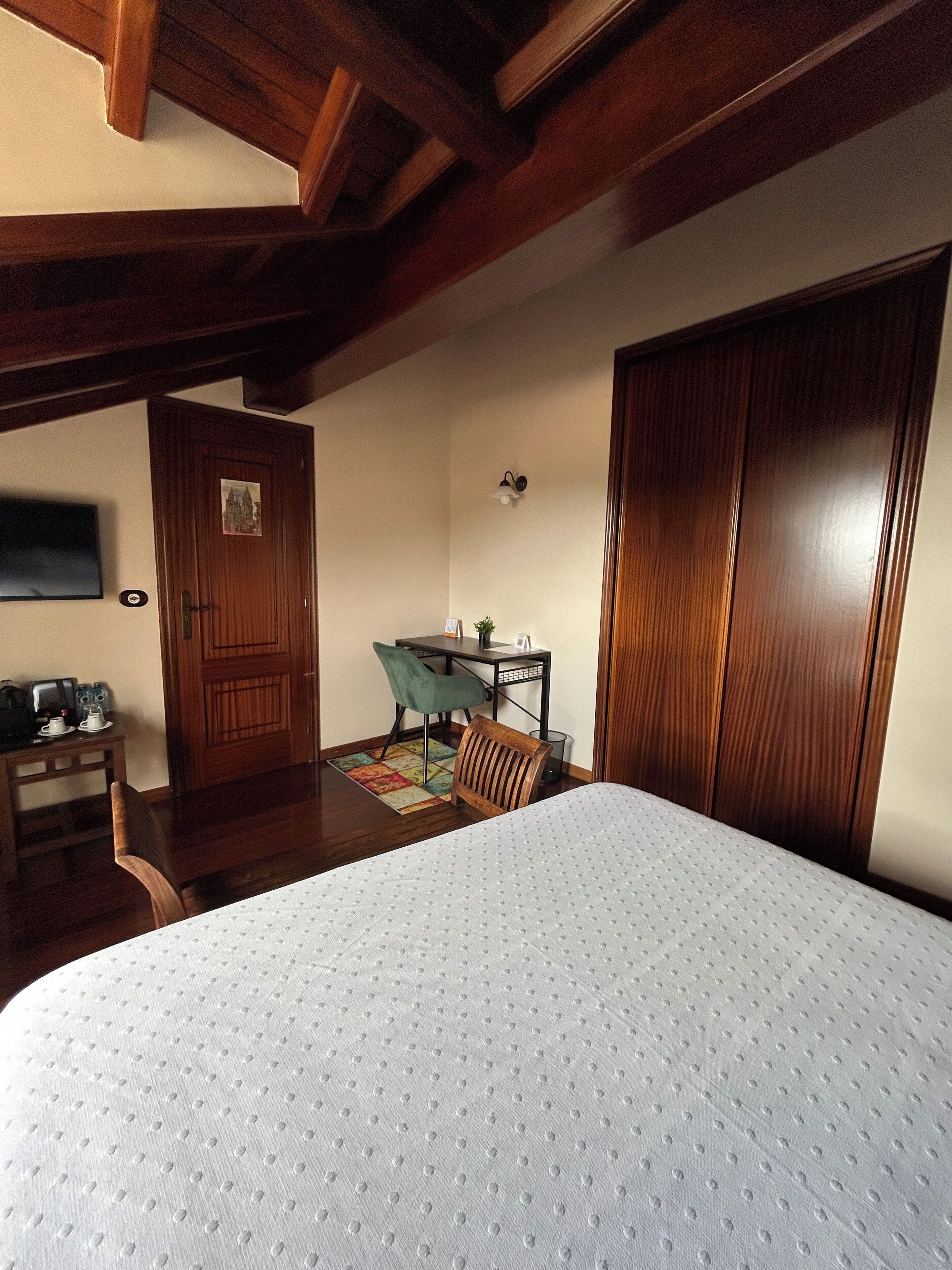 Un dormitorio con cama, armario de madera, escritorio, silla y una mesita con una planta.