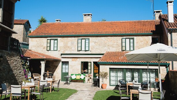 A stone building with a tiled roof, outdoor seating area with tables and chairs, and a pathway leading to the entrance. - CASA DE COSTOIA (Ames)
